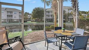 Une terrasse avec une table et des chaises, donnant sur un plan d’eau et des immeubles résidentiels.