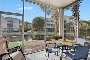 A patio with a table and chairs, overlooking a body of water and residential buildings. - Willow Bend 214: 1st Floor End Unit in Barefoot! New On Program! (North Myrtle Beach)