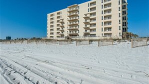 Un hotel de varios pisos con balcones, situado en una playa de arena.