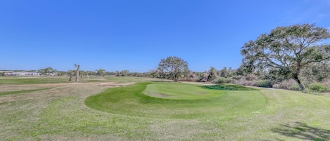 Un parcours de golf avec un gazon bien entretenu, des arbres et un ciel bleu dégagé.