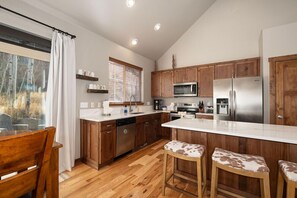A modern kitchen with wooden cabinets, stainless steel appliances, and a bar area with stools. - Luxurious 4 bed, private HT, sleeps 12, ski-in/ski-out access (Granby)