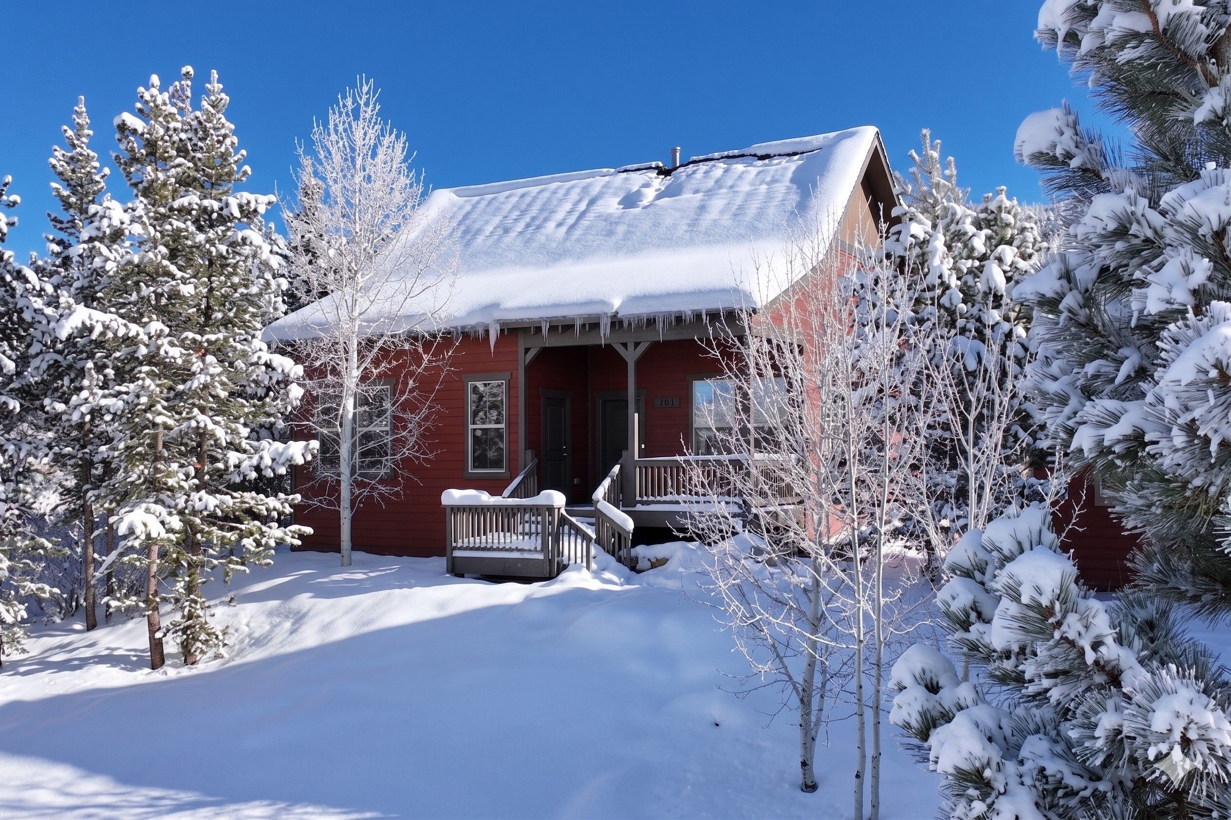 Une cabane recouverte de neige, avec une façade rouge, un porche et un ciel bleu clair.
