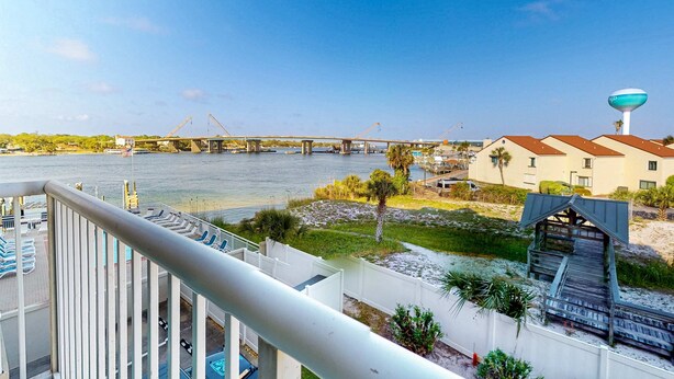 A view from a balcony overlooking a river, a bridge, and a beach with a water tower. - Palm Court Yacht Club 312A - Third-floor cozy coastal studio with soundviews, WiFi, and shared pool & hot tub (Fort Walton Beach)