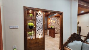 Um balcão de recepção de madeira com um painel decorativo, plantas em vasos e uma parede com padrão no fundo.