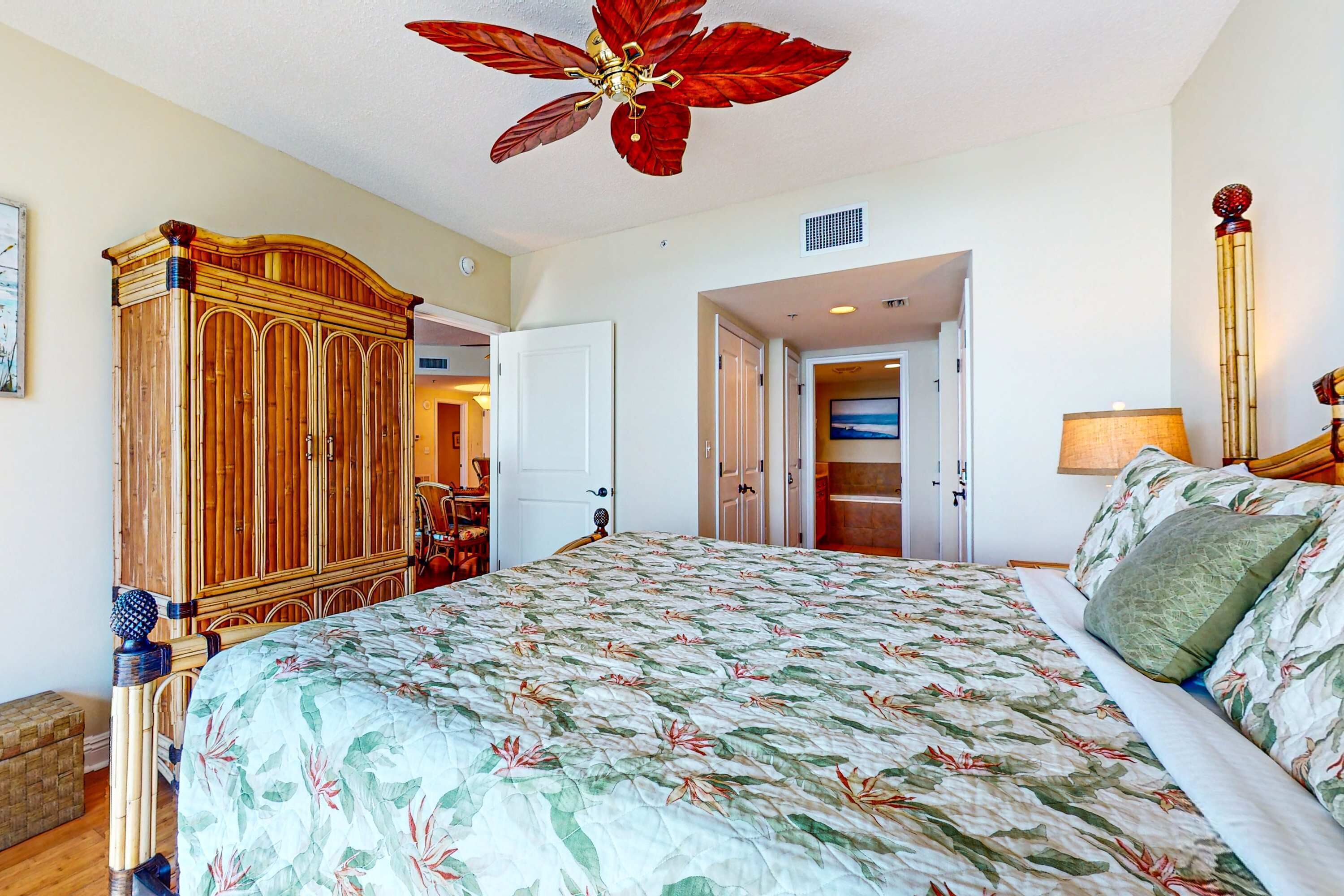 Une chambre à coucher avec un grand lit, une armoire, un ventilateur de plafond et une porte donnant sur une autre pièce.