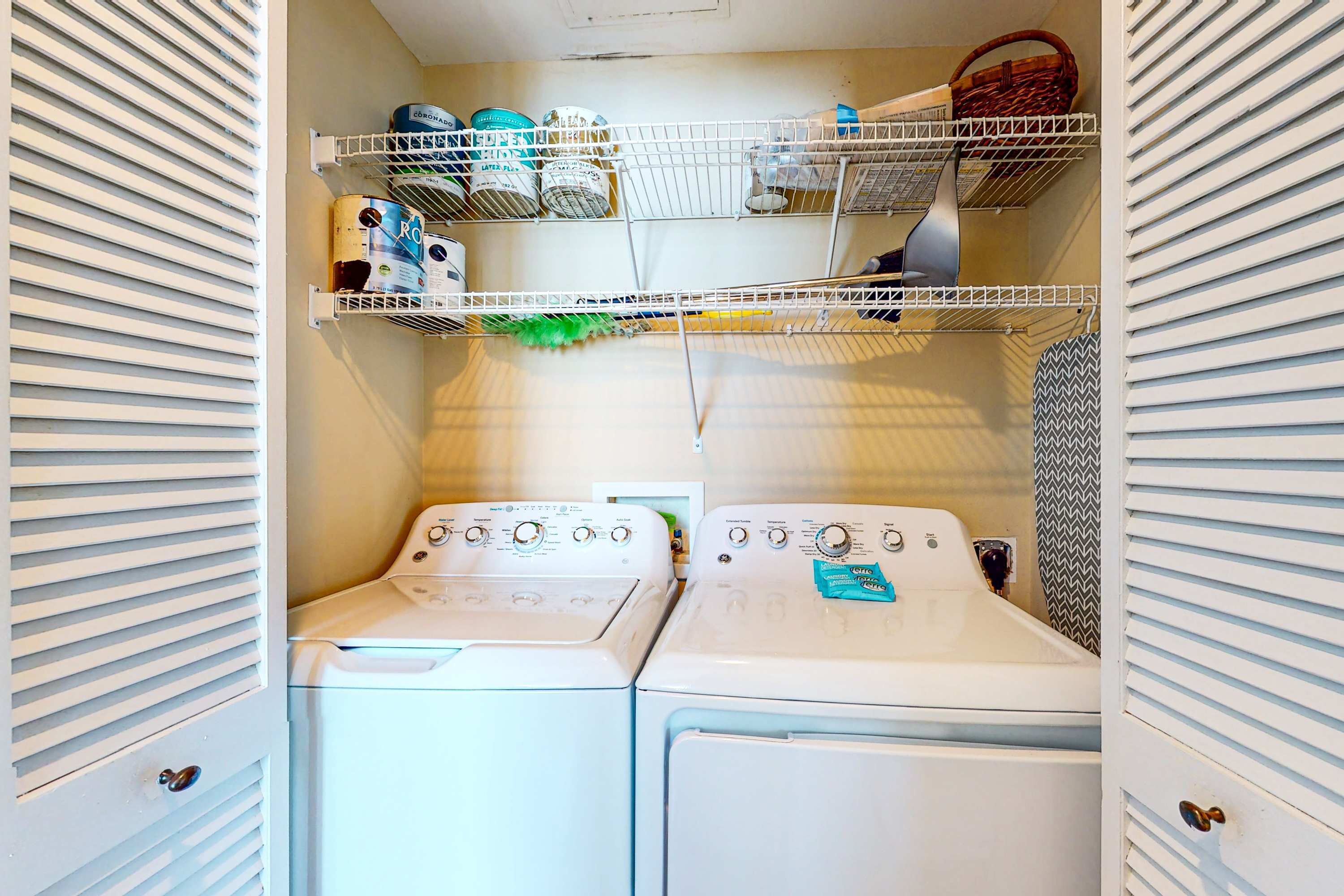 Une buanderie équipée de deux machines à laver et deux sèche-linge superposés, avec des étagères au-dessus pour ranger divers objets, et un rideau de douche à motifs.