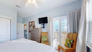Un dormitorio con una cama grande, televisión, cómoda y una silla de mimbre.