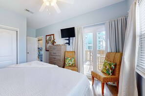 A bedroom with a large bed, a television, a dresser, and a wicker chair. - Sound-front home with fishing dock, balcony, sundeck & easy beach access (Pensacola Beach)
