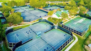 Ein Luftbild eines Sportkomplexes mit mehreren Tennisplätzen, umgeben von Bäumen und Gebäuden.