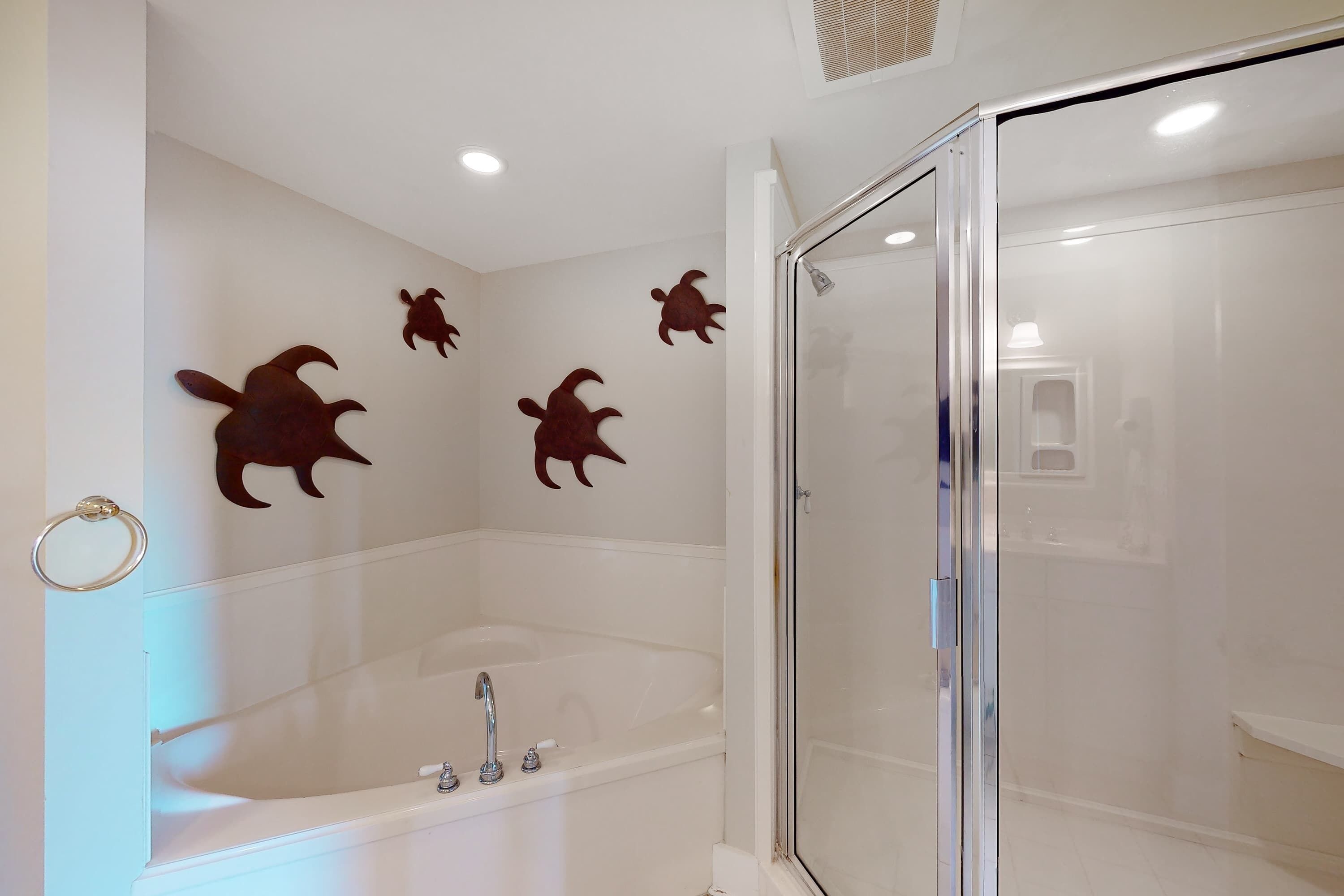 A bathroom with a bathtub, a glass shower enclosure, and wall-mounted turtle decorations.