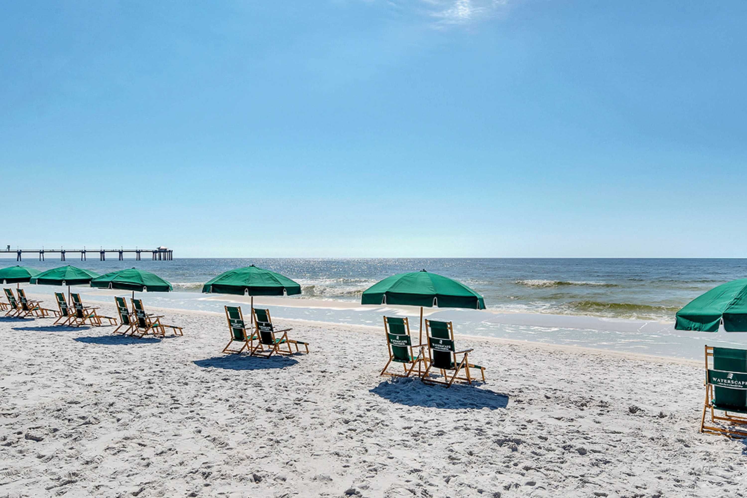 Une plage bordée de rangées de parasols verts et de chaises longues en bois.