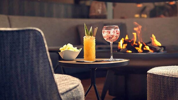 Un'accogliente area salotto con un tavolino rotondo, un drink e una candela, una ciotola di snack e un braciere sullo sfondo.