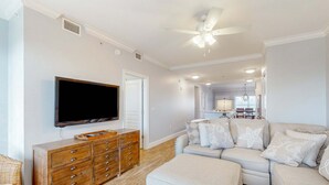 Ein Wohnzimmer mit Flachbildfernseher, Holzkommode, beiger Couch und Deckenventilator.