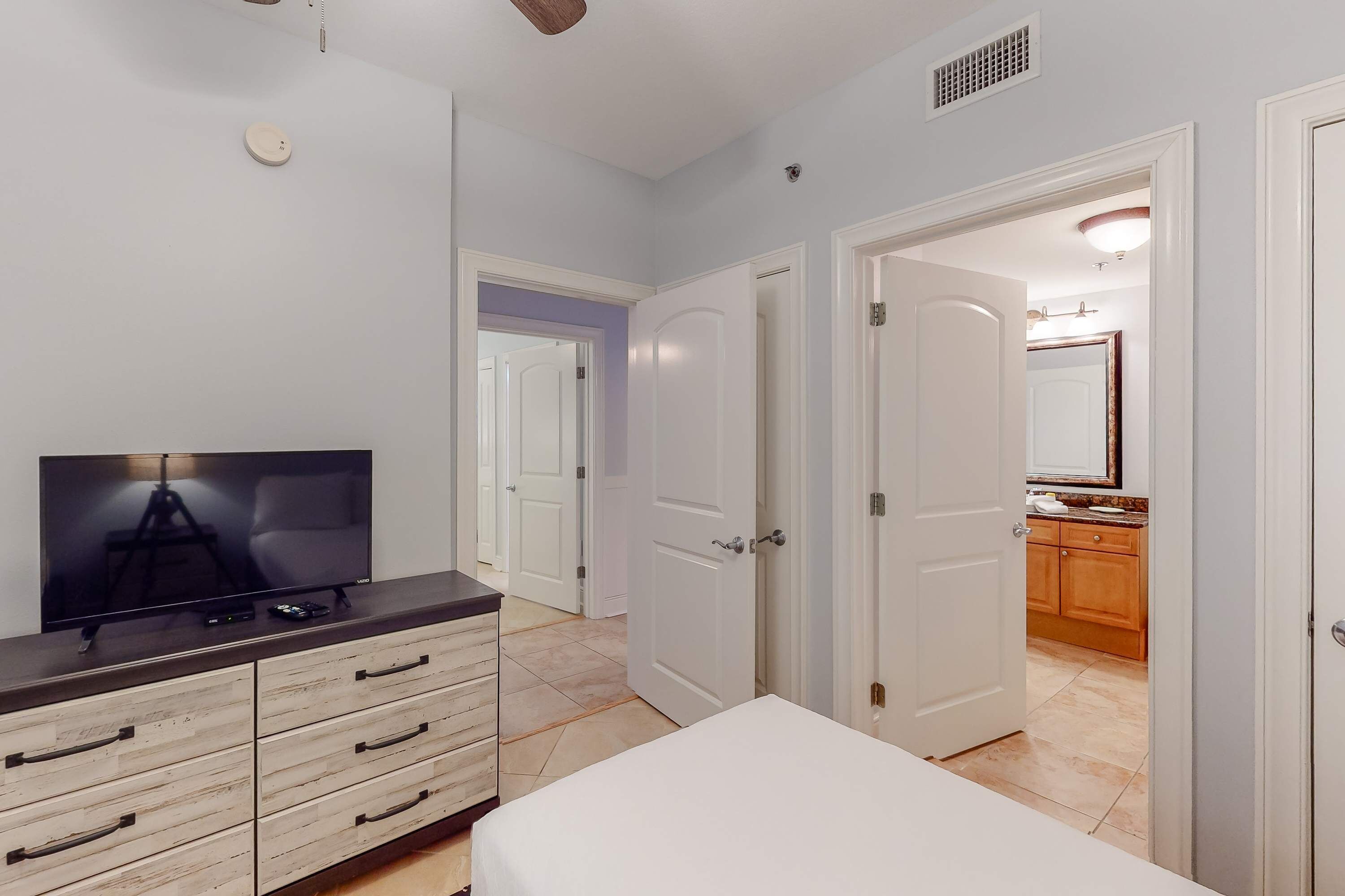 Une chambre à coucher avec une télévision, une commode en bois et un lit blanc.
