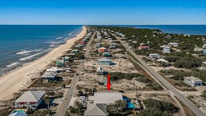 Une vue aérienne d’une zone côtière, avec une longue étendue de plage, des rangées de maisons et une route qui longe le rivage.
