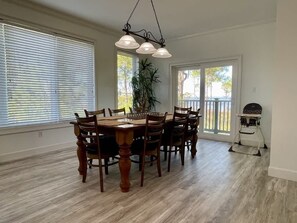 A dining area with a wooden table and chairs, large windows, and a ceiling light fixture. - Discount Summer, Bay-view, dog-friendly, outdoor pool, elevator, decks, dock access & W/D (St. George Island)