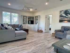 A spacious living room with a grey sofa, a coffee table, and a built-in entertainment unit. - Discount Summer, Bay-view, dog-friendly, outdoor pool, elevator, decks, dock access & W/D (St. George Island)
