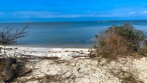 Ein Strand mit klarem, blauem Wasser, einem sandigen Ufer und einem Pier in der Ferne.