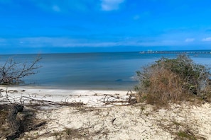 A beach with clear blue water, a sandy shore, and a pier in the distance. - Discount Summer, Bay-view, dog-friendly, outdoor pool, elevator, decks, dock access & W/D (St. George Island)