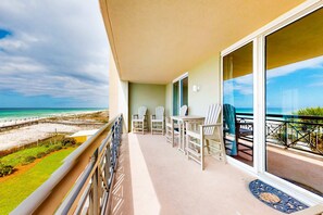 Een balkon met uitzicht op het strand, een tafel met stoelen en een deur naar een overdekt gebied.
