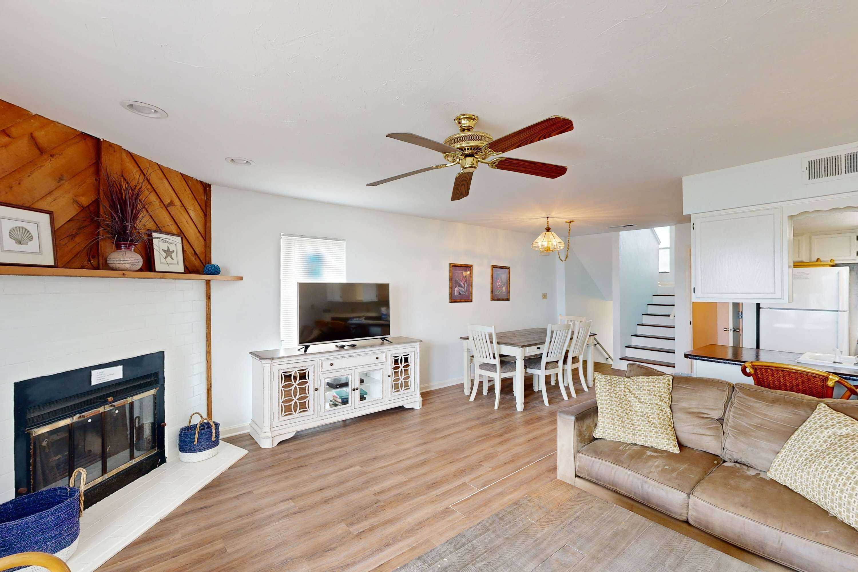 A spacious living room with a fireplace, a ceiling fan, a dining area, and a kitchen visible through an open door.
