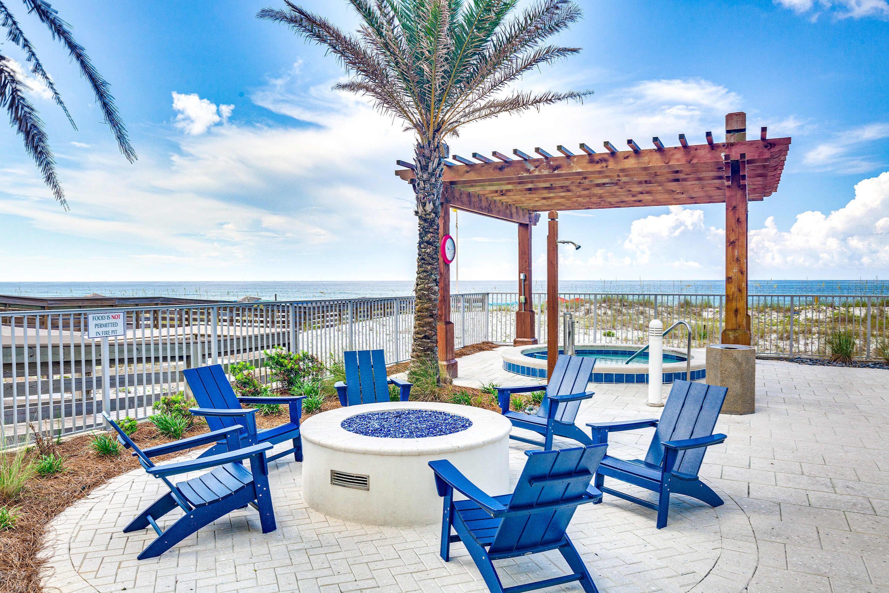 An outdoor seating area with Adirondack chairs, a fire pit, and a wooden pergola overlooking the ocean.