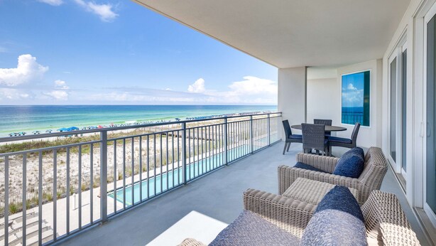 A balcony with wicker furniture, a pool, and a view of the beach and ocean. - Blu 301 - Third-floor, Gulf-view condo with pool and hot tub access, central AC, & W&D (Fort Walton Beach)