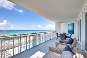 Un balcon agrémenté de meubles en osier, une piscine et une vue sur la plage et l’océan.