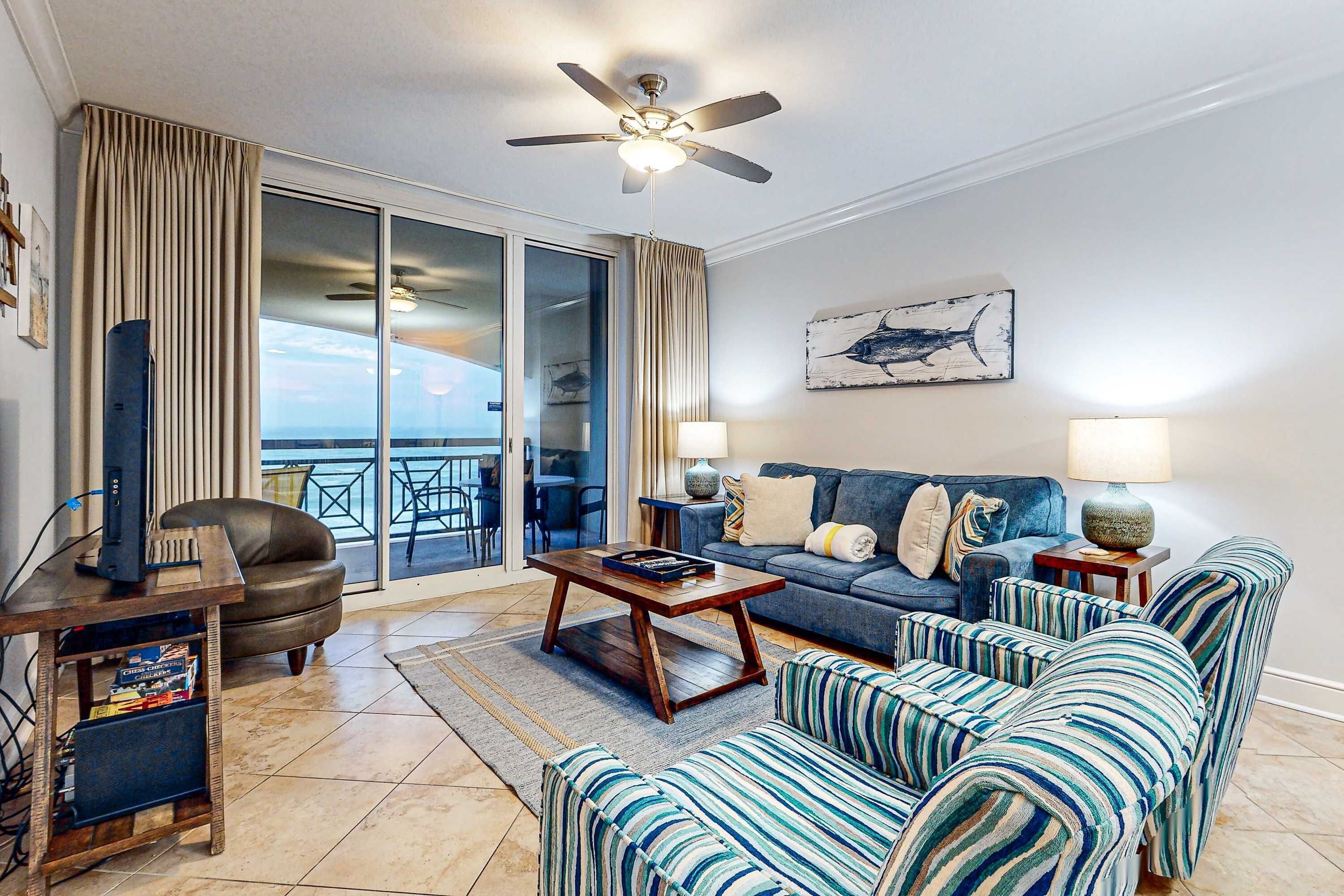 A living room with a sofa, armchairs, a coffee table, a TV on a stand, and a ceiling fan.