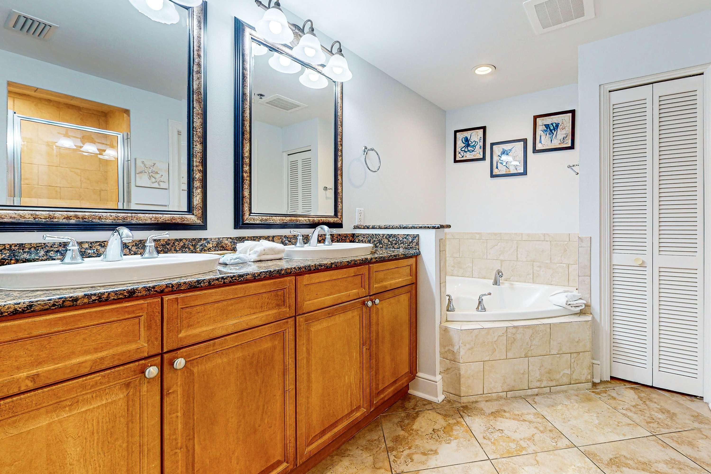 A bathroom with a double sink vanity, a bathtub, and a large mirror with lights.