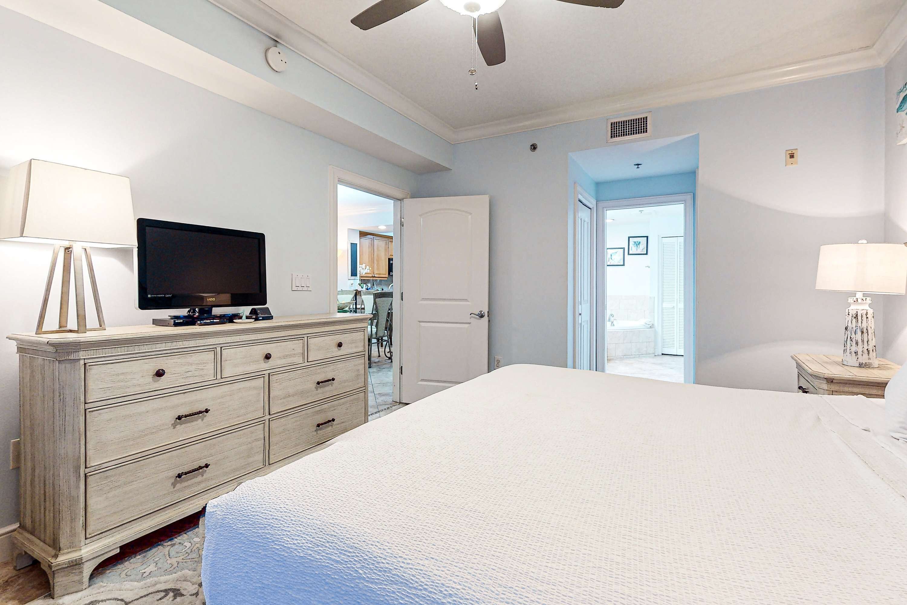 Une chambre à coucher comprenant un lit, une commode, un téléviseur et un ventilateur de plafond.