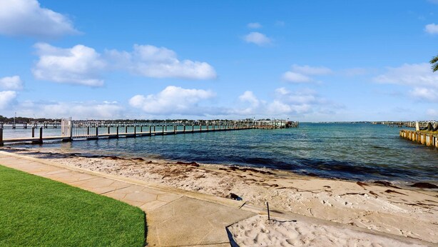 A waterfront promenade with a concrete walkway, a grassy area, and a wooden pier extending into the water. - Cozy sound side condo with shared pool, Close to shopping and beach (Fort Walton Beach)