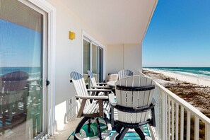 A balcony with a view of the beach, featuring two Adirondack chairs and a small table. - Gulf Dunes 512 - Beachfront condo with gulf views, pool, & balcony - near dining,attractions (Fort Walton Beach)