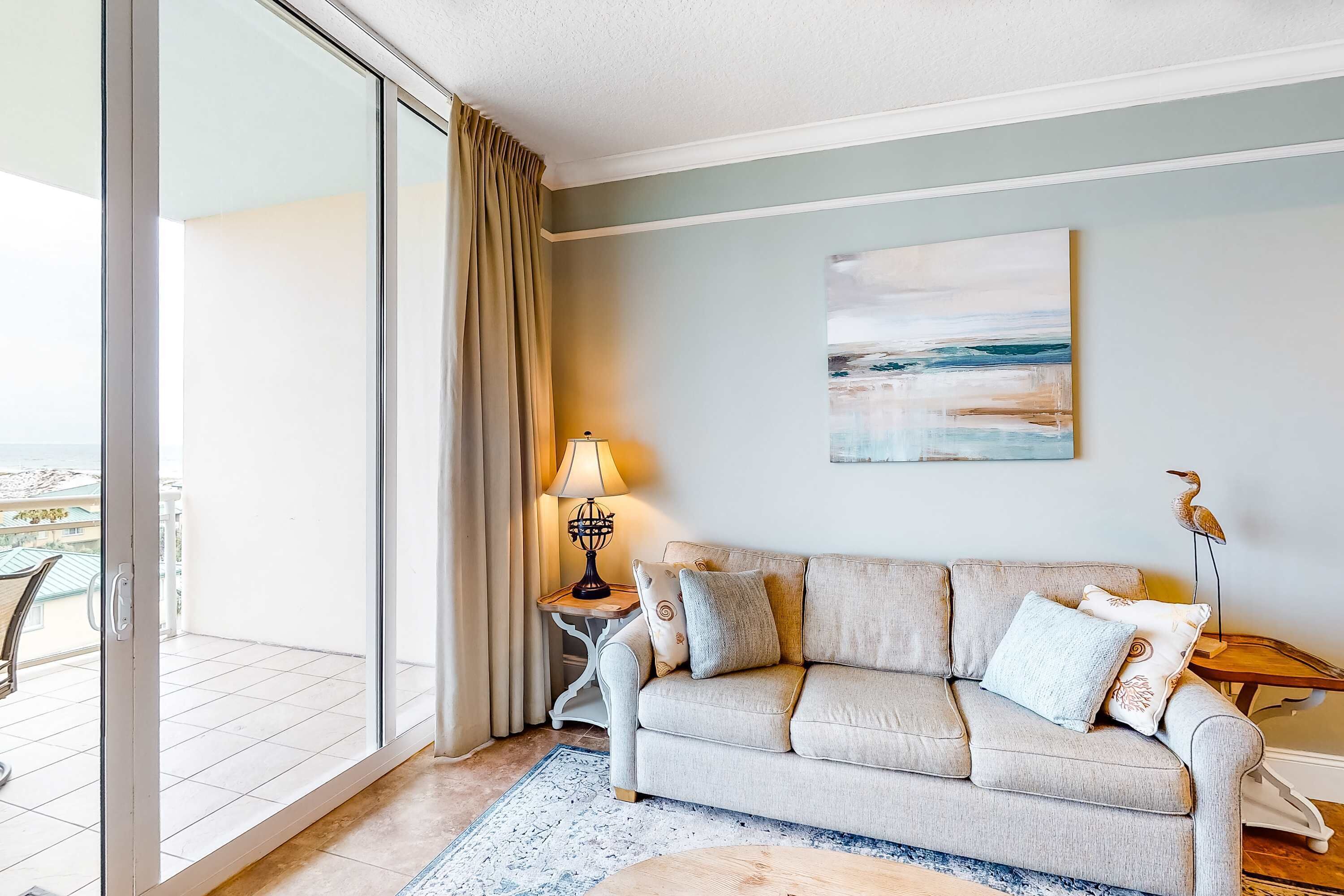 Een woonkamer met een bank, een lamp, een schilderij en uitzicht op buiten.