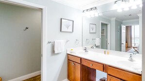 Un baño con un tocador blanco, un espejo grande y una puerta que da a otra habitación.