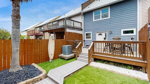 Ein Wohnhaus mit Holzterrasse, kleiner Terrasse und umzäunter Garten.