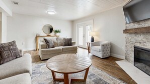 Ein Wohnzimmer mit Kamin, einem runden Couchtisch, einer Couch und einem an der Wand montierten Fernseher.