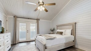 Ein Schlafzimmer mit Bett, Deckenventilator, Nachttisch, Kommode und Fenster mit Vorhängen.