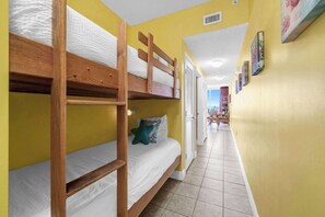 Ein Etagenbett in einem Zimmer mit gelben Wänden, Fliesenboden und Meerblick durch eine offene Tür.
