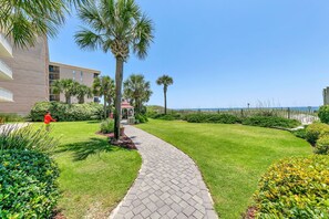 A well-maintained garden pathway leading to a building with a beach view. - Beach Chic Condo On Okaloosa Island Gulfside Pool & Exercise Room (Fort Walton Beach)