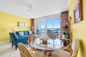 A living room with a blue sofa, wicker chairs, a glass coffee table, and a ceiling fan. - Beach Chic Condo On Okaloosa Island Gulfside Pool & Exercise Room (Fort Walton Beach)