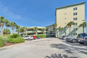 A parking area with multiple cars, a building with balconies, and palm trees. - Beach Chic Condo On Okaloosa Island Gulfside Pool & Exercise Room (Fort Walton Beach)