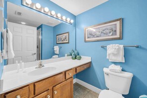 A bathroom with a white sink, wooden cabinets, a white toilet, and blue walls. - Beach Chic Condo On Okaloosa Island Gulfside Pool & Exercise Room (Fort Walton Beach)
