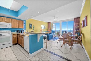 A modern kitchen with a blue accent wall, wooden cabinets, and a central island. - Beach Chic Condo On Okaloosa Island Gulfside Pool & Exercise Room (Fort Walton Beach)