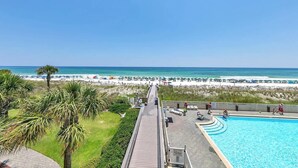 Un resort con piscina, vista a la playa y un muelle de madera que conduce a la playa.