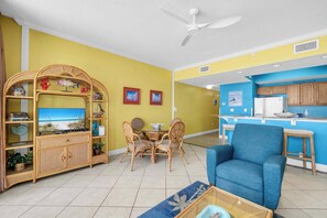 Ein Wohnzimmer mit Essbereich, einem blauen Sessel, einem Deckenventilator und einer Küche mit Holdekor.
