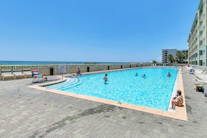 Una piscina con vista despejada al océano, rodeada de sillas de descanso y un edificio.