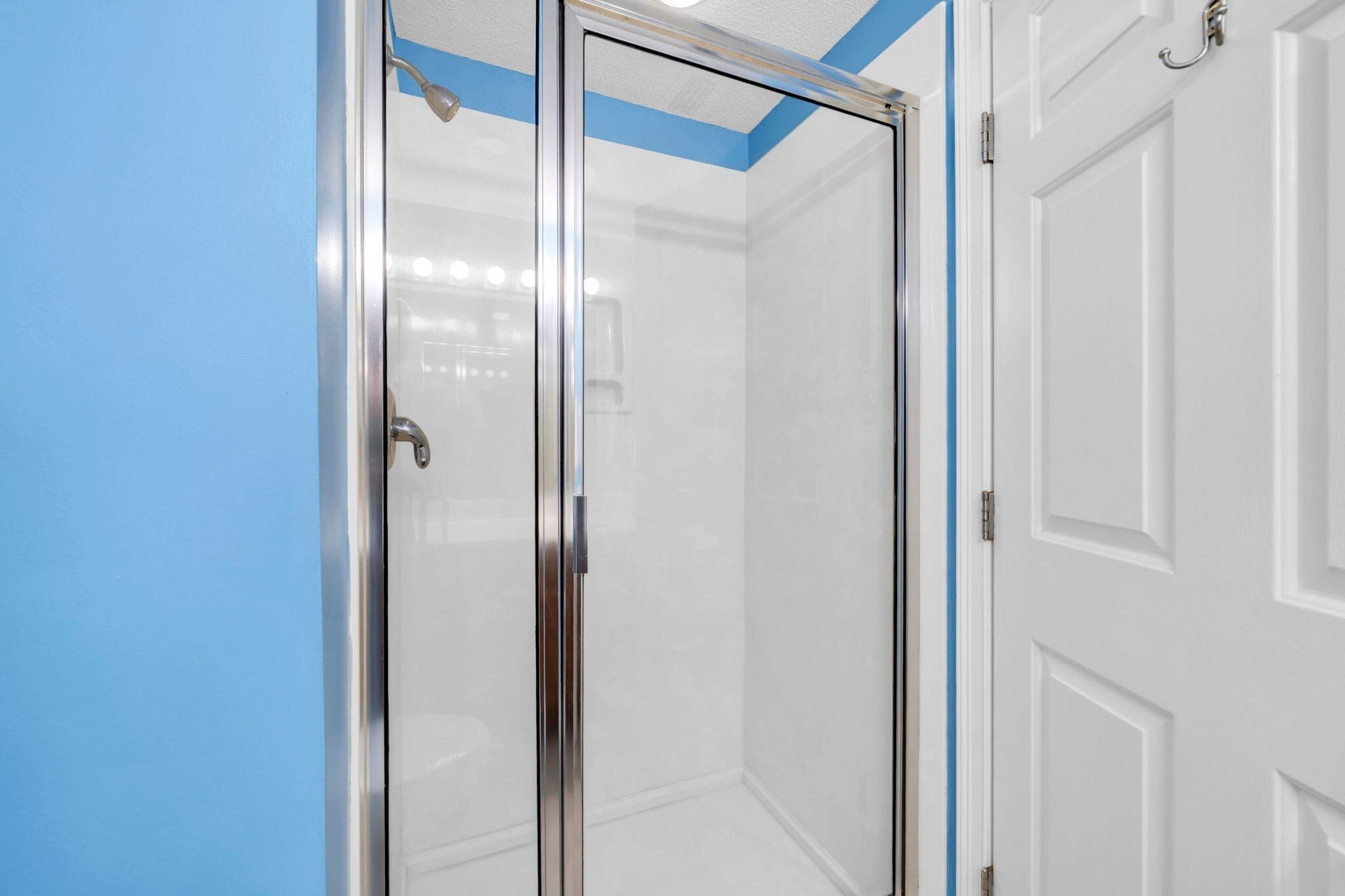 Un bagno con box doccia in vetro, una porta bianca e una parete azzurra.