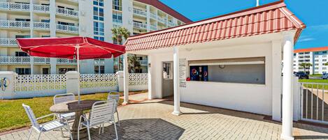 A patio area with a table and chairs, a red umbrella, and a kiosk with a Pepsi sign.