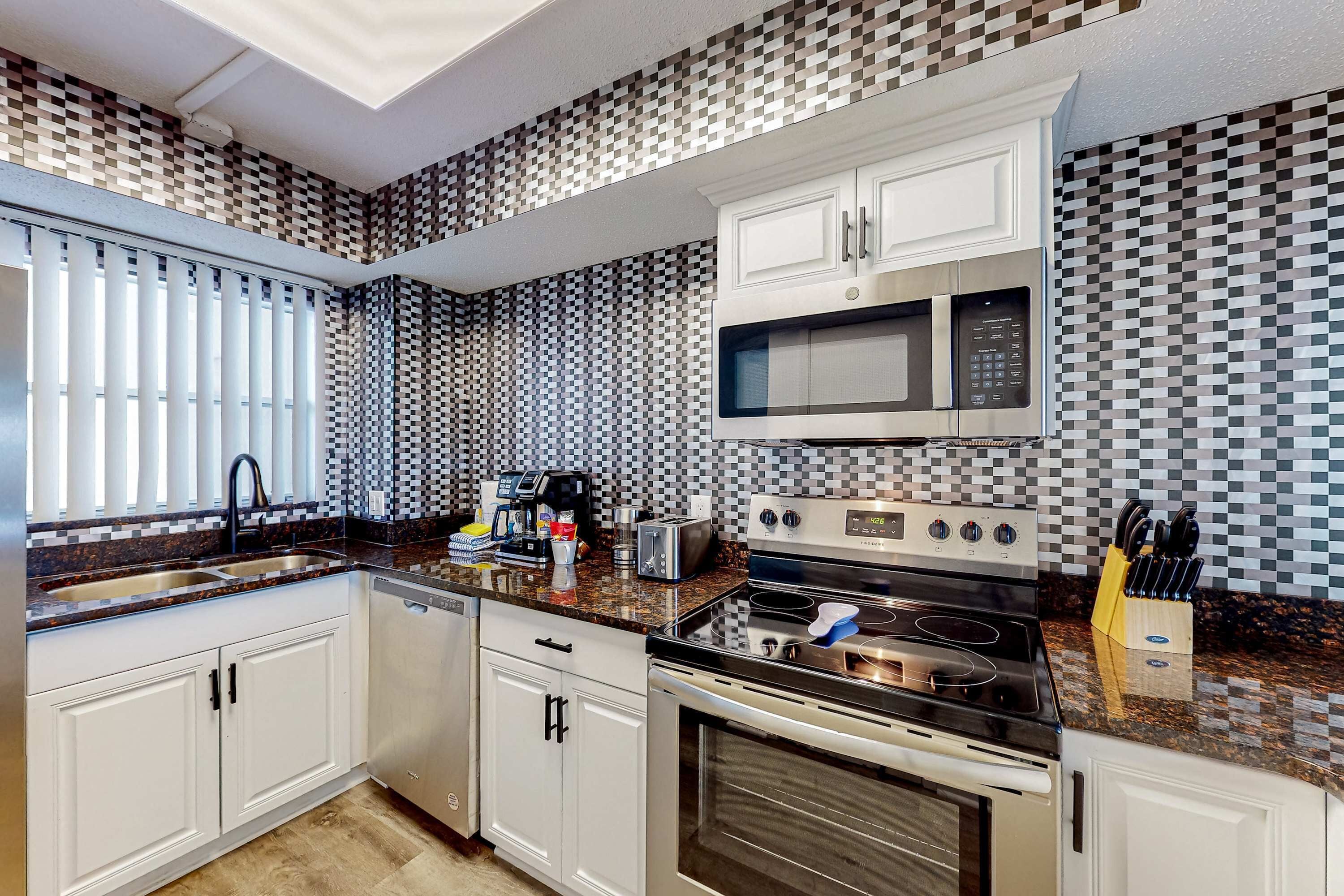 A modern kitchen with white cabinets, a granite countertop, a microwave, an oven, and a coffee maker.